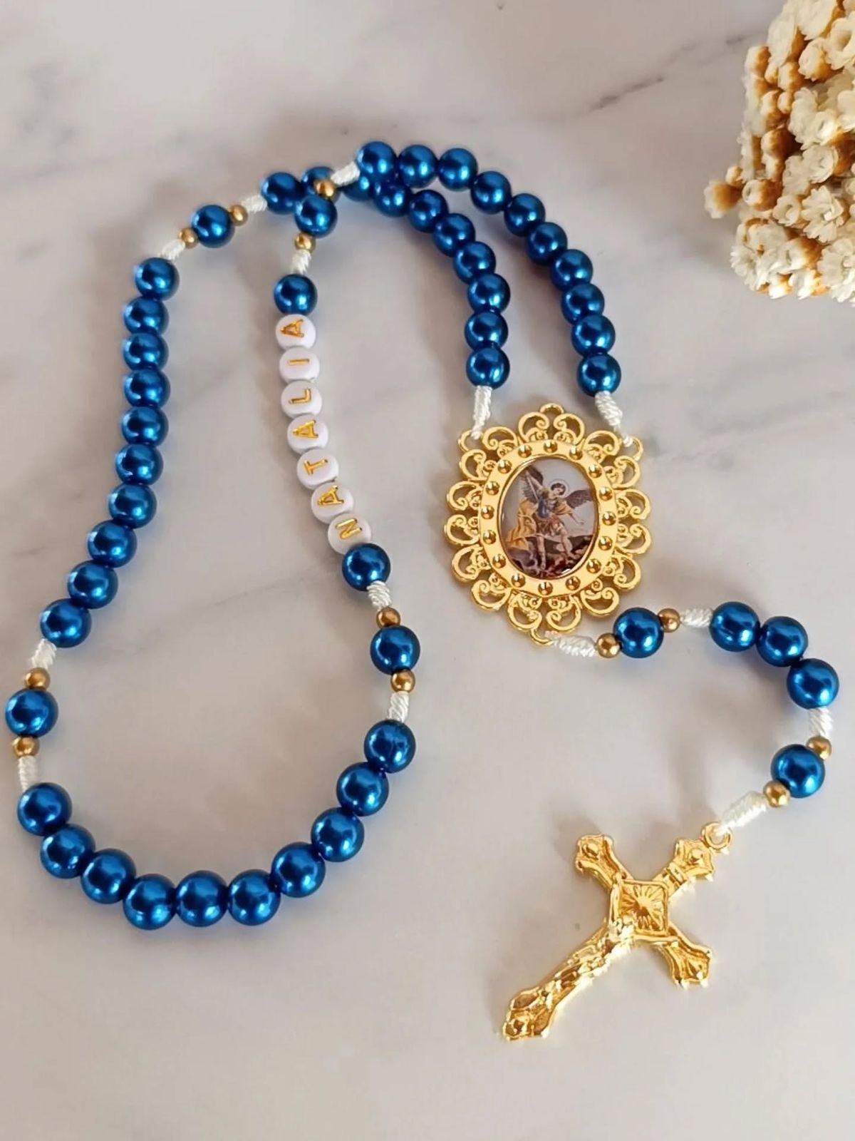 Terço artesanal azul personalizado com nome e medalha dourada, fotografia editorial